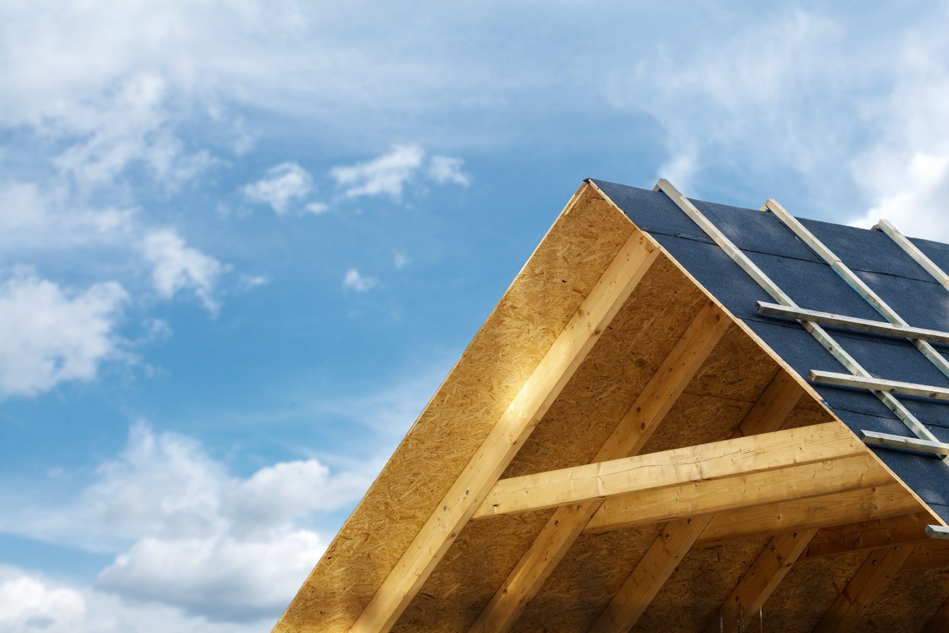Close-up of a wooden roof frame under construction against a blue sky with clouds.