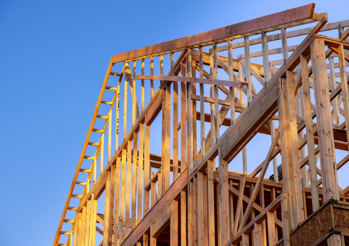 Wooden frame structure of a house under construction against a clear blue sky.