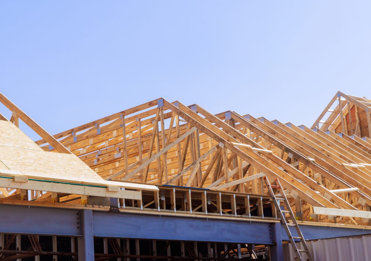 Wooden framework of a house roof under construction against a clear blue sky.
