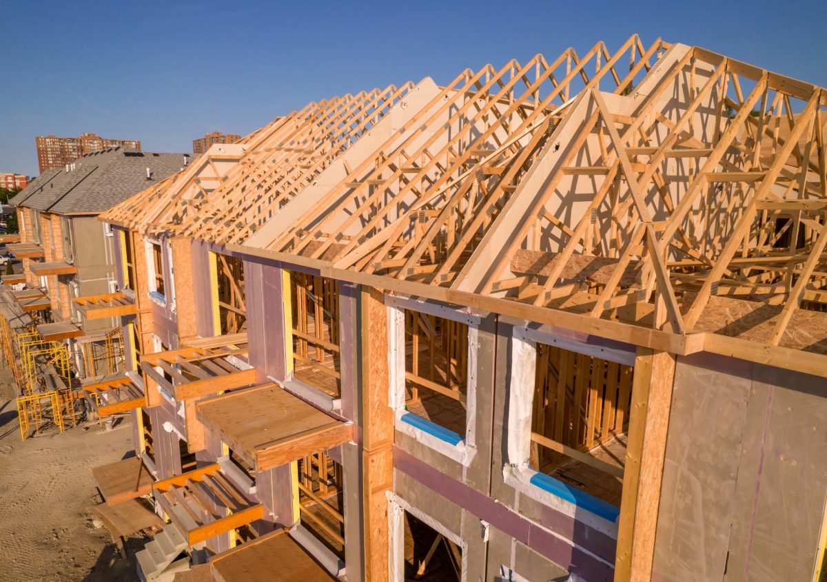 Wooden framework of houses under construction with exposed roof trusses on a sunny day.