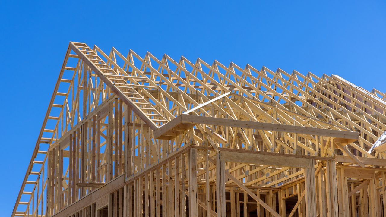 Wooden framework of a house under construction against a clear blue sky.