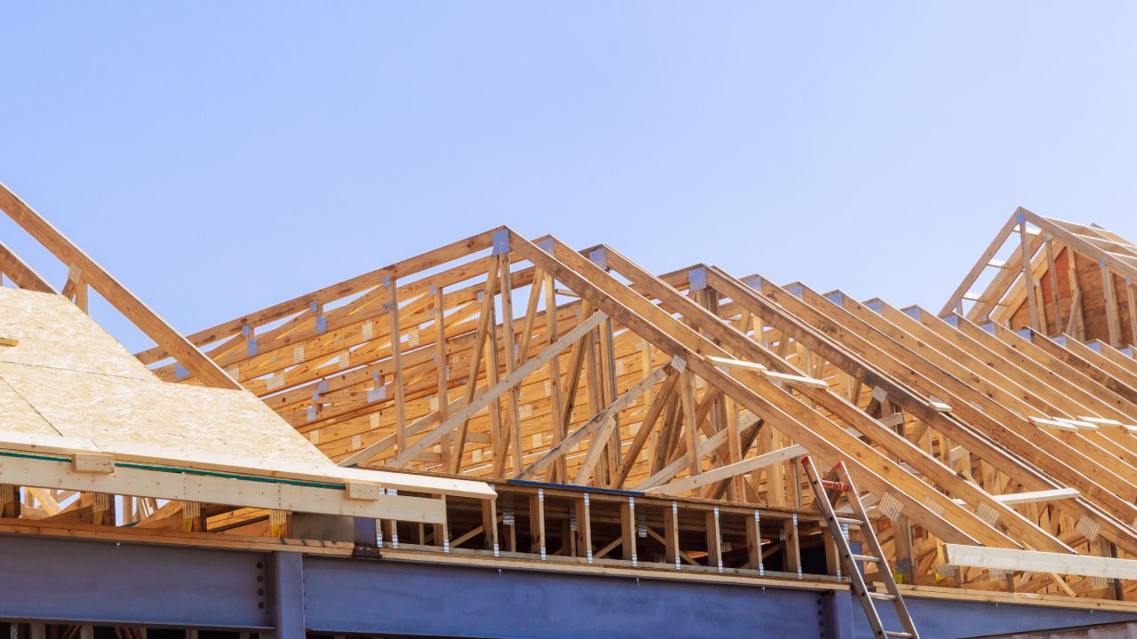 Wooden framework of a roof under construction against a clear blue sky.